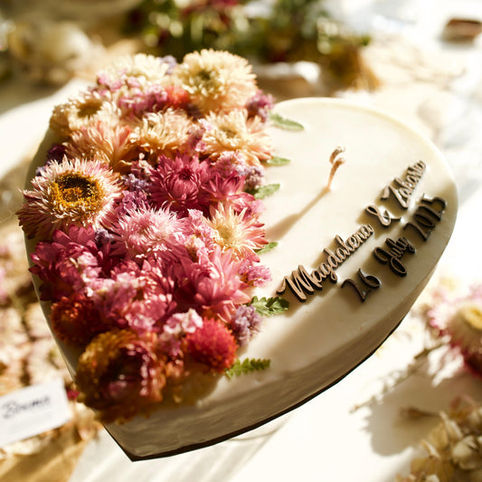Decorative candle with floral elements and text on a stand, surrounded by flowers.