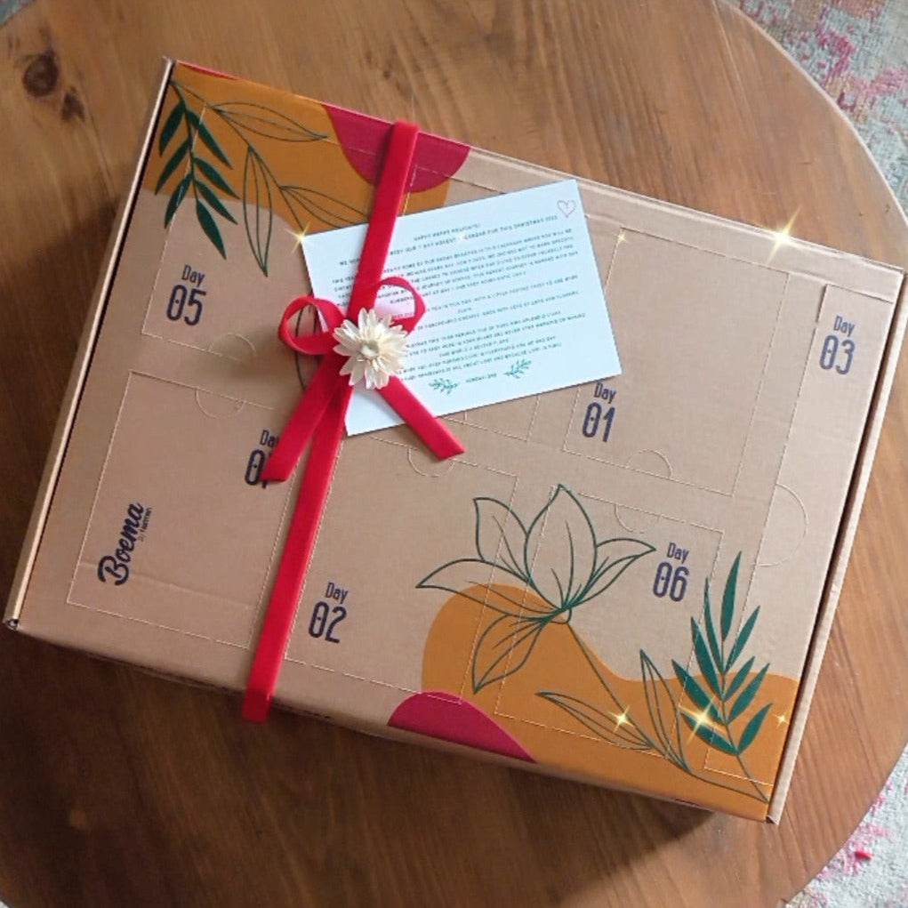 A decorative advent calendar box with a red ribbon bow on top, featuring floral patterns placed on a round wooden table.