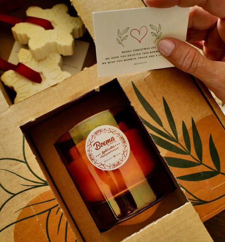 Person holding a card over a box with a candle inside, featuring a brand label.