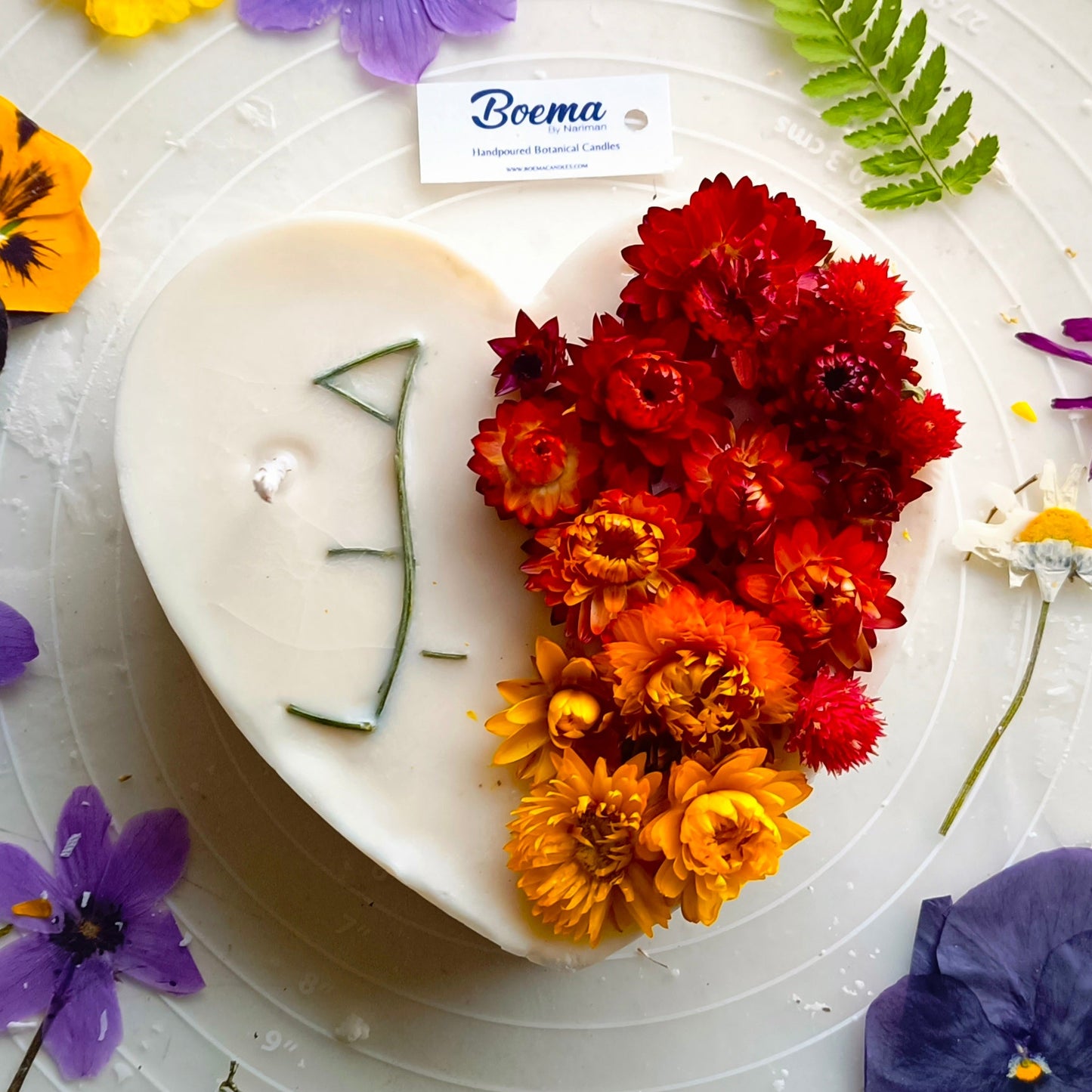 Heart-shaped candle with flowers and the word hobb or love made with flowers