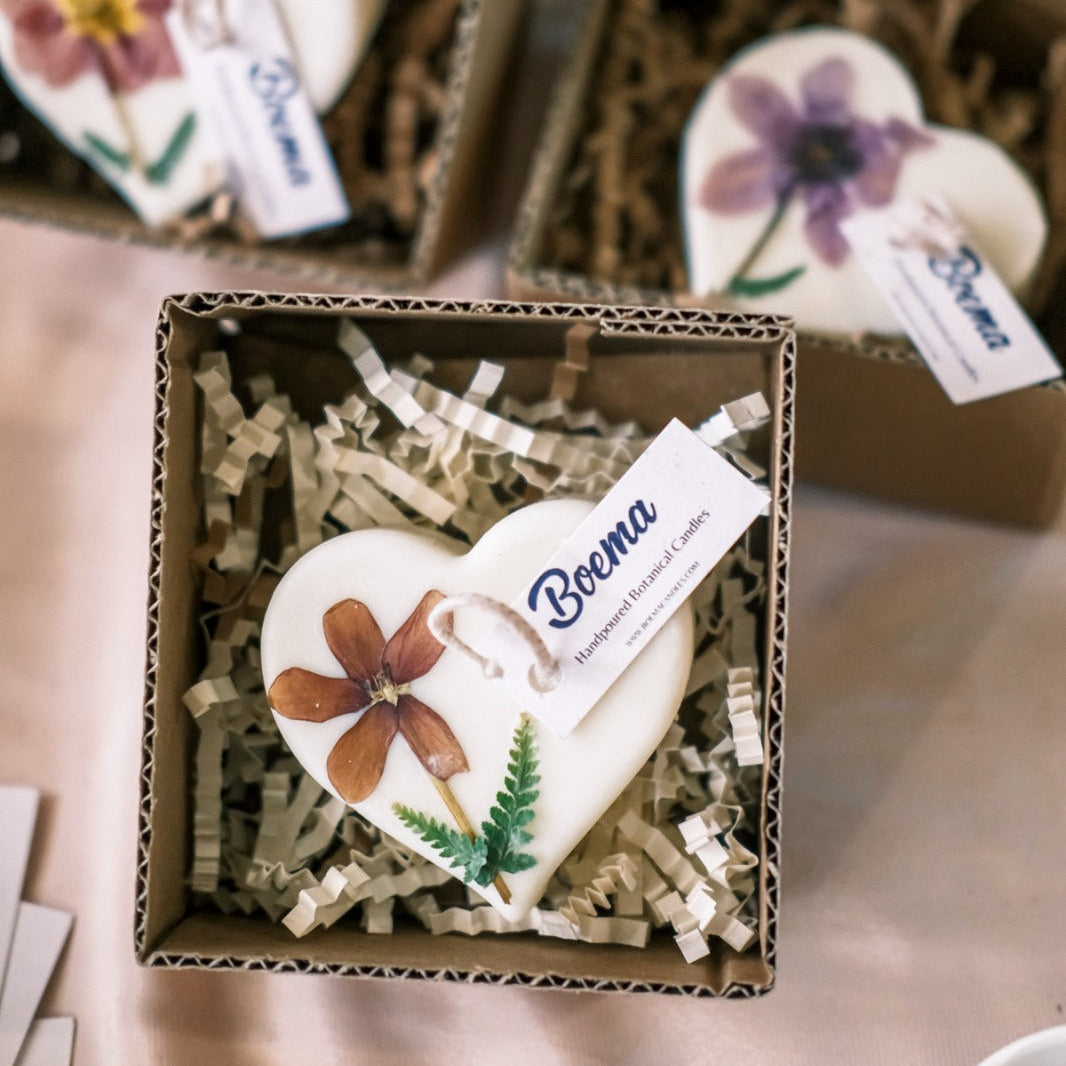 Heart-shaped candles with floral designs in a box on a table.